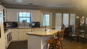 A kitchen with white cabinets, a central island, and a dining area with chairs. - Sylvan Lakes Quiet Place (West Monroe)