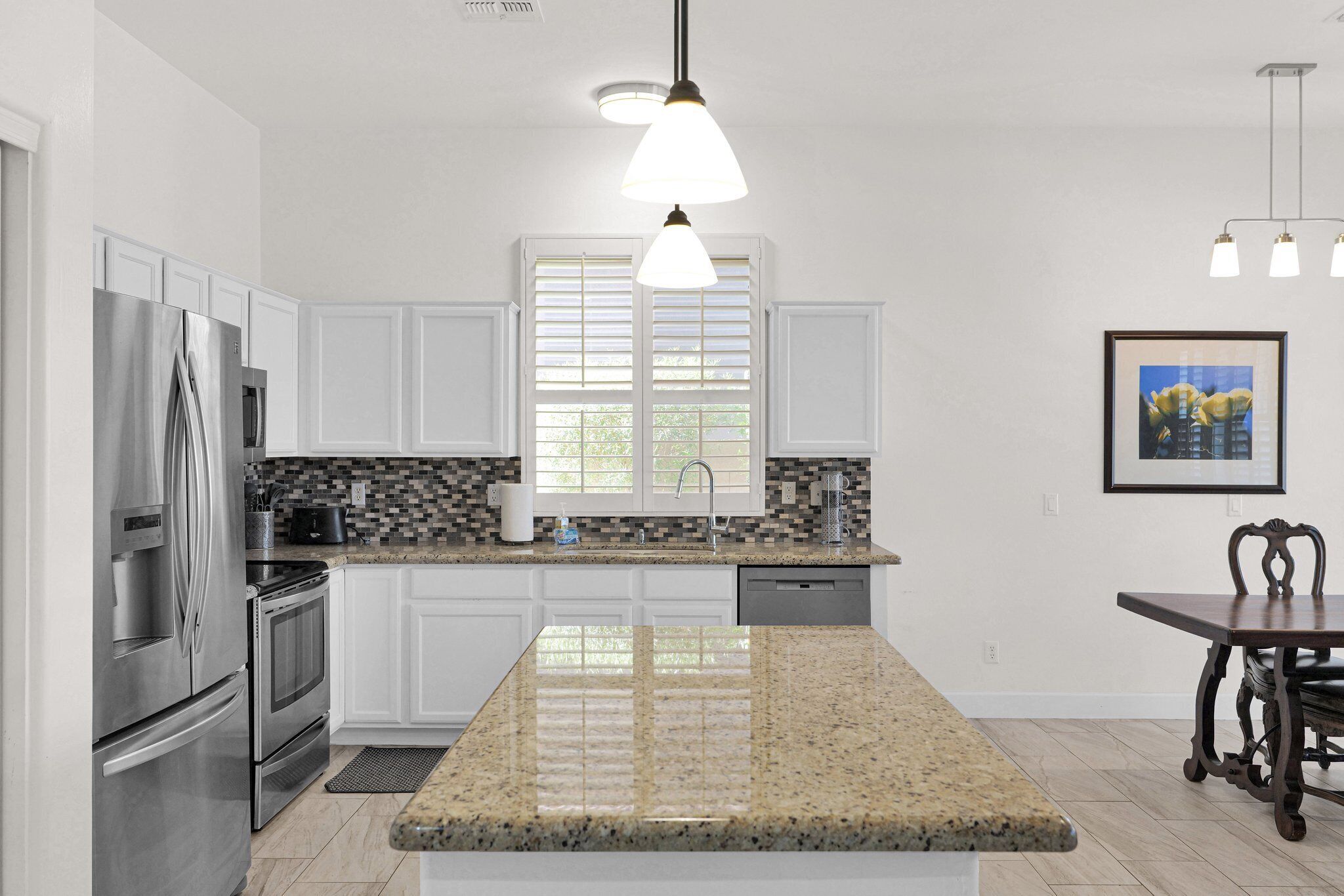 A modern kitchen with white cabinetry, stainless steel appliances, a granite countertop, and pendant lighting.