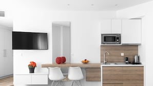 A modern kitchen with a flat-screen TV, a microwave, and a sink. There are two white chairs and a small table with a potted plant. - Hermes Nilie Hospitality MGMT (Thessaloniki)