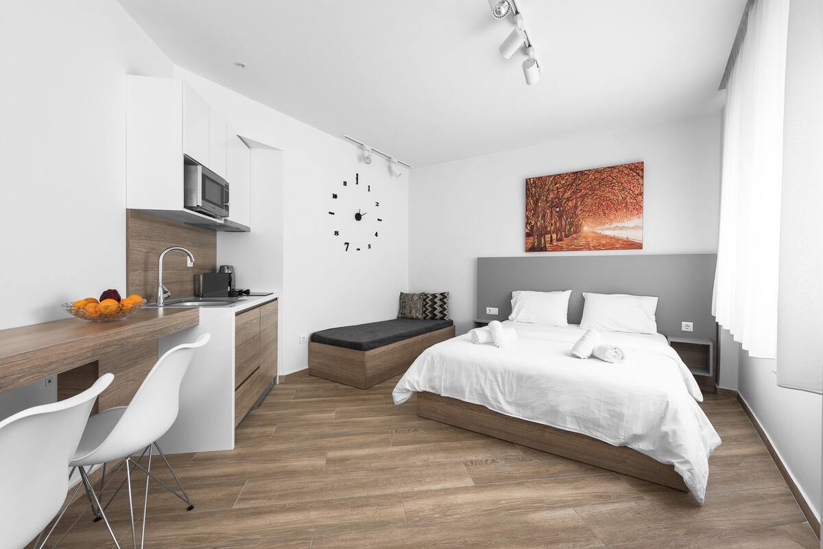 A modern, compact bedroom with a bed, bedside table, and a small seating area.