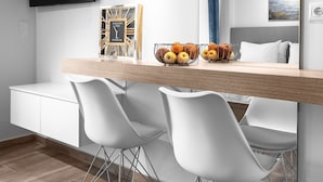A modern hotel room with a wooden dining table, white chairs, a flat-screen TV, and a large mirror reflecting the room. - Hermes Nilie Hospitality MGMT (Thessaloniki)