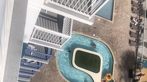 Vue aérienne d’une piscine au design sinueux, entourée de chaises longues et de parasols.
