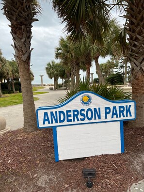 Schild für Anderson Park, mit freiem Blick auf die umliegenden Palmen und ein entferntes Gewässer.