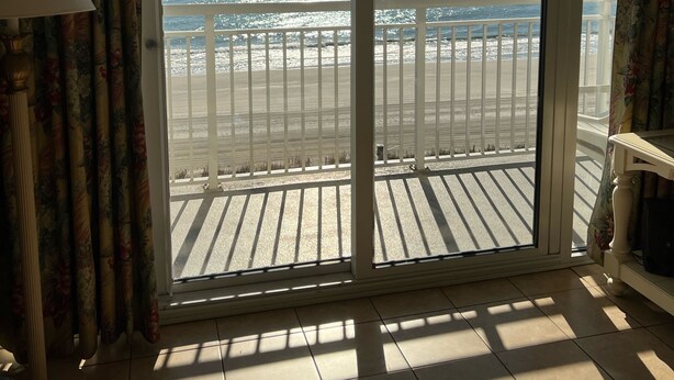 Une pièce dotée d’une grande porte-fenêtre coulissante donnant sur un balcon avec vue sur la plage et l’océan.