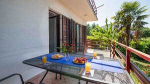 An outdoor dining area with a table set for two, featuring a blue placemat, plates of fruit, and glasses of orange juice.