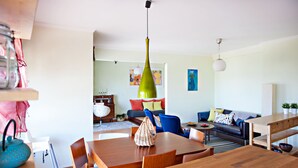 A modern living room with a wooden dining table, blue chairs, a black sofa, and a colorful abstract painting on the wall. - Magnificent view (Faro)