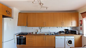 A kitchen with wooden cabinets, a refrigerator, oven, microwave, sink, and a washing machine. - Magnificent view (Faro)