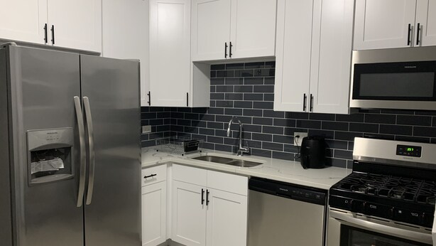 Una cocina moderna con gabinetes blancos, un refrigerador de acero inoxidable, un salpicadero de azulejos negros, un fregadero, un lavavajillas y una estufa.