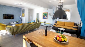 Una sala moderna con una mesa de comedor de madera, sofá de estampado amarillo y verde, y una lámpara colgante negra.