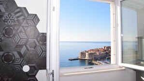 Habitación con ventana que da a una ciudad costera, con una pared de patrón hexagonal y vistas a un puerto histórico.
