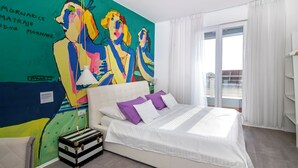 Una habitación de hotel moderna con una cama grande, un mural colorido y un balcón con vistas.