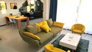 Una sala de estar moderna con un sofá, dos sillones amarillos, una mesa de comedor y una zona de cocina al fondo.