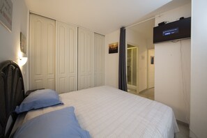 Un dormitorio con cama, armario, televisor y puerta que da a otra habitación.