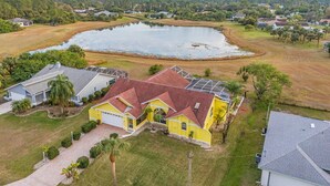 A residential area with a large pond, houses with solar panels, and a yellow house with a red roof. - The Yellow | Lakefront Home, Heated Pool & Spa (Leigh Acres)