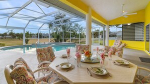 An outdoor dining area with a pool view, yellow walls, and patterned furniture. - The Yellow | Lakefront Home, Heated Pool & Spa (Leigh Acres)
