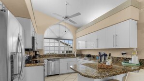 A modern kitchen with white cabinets, a granite countertop, and stainless steel appliances. - The Yellow | Lakefront Home, Heated Pool & Spa (Leigh Acres)
