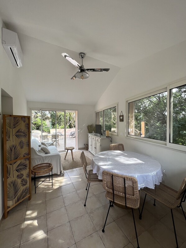 A spacious room with a dining area, a ceiling fan, a large window, and a view of the outdoors. - Cozy accommodations, within walking distance of the beach, private terrace (Porto-Vecchio)