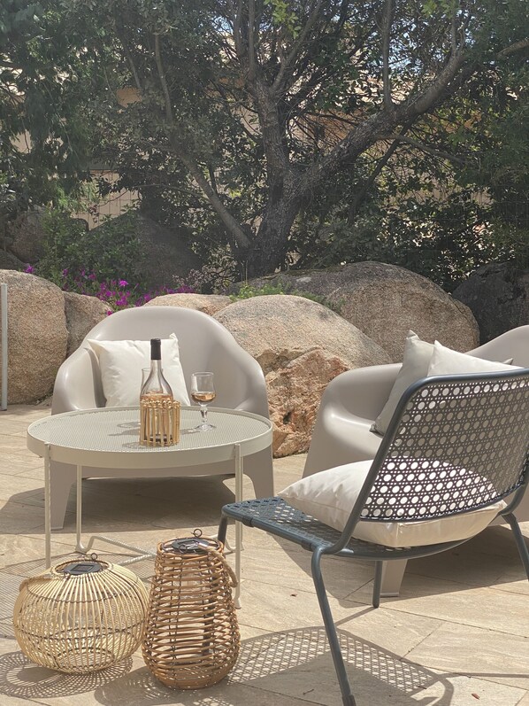 An outdoor seating area with two round tables, wicker chairs, and large rocks. - Cosy accommodation, walking distance to the beach, private terrace (Porto-Vecchio)