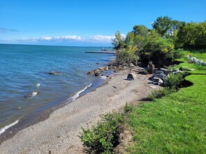 A pebbled beach with a grassy area and trees, a lighthouse in the distance, and calm water. - Grimsby Lakeview Suite l 2 Min Walk to Lake Ontario l King Bed l Great Value (Grimsby)