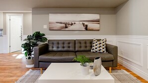 Un salon avec un canapé en cuir marron, une table basse blanche et un grand tableau encadré représentant une jetée, accroché au mur.