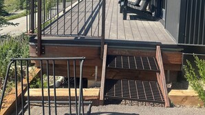 Moderni rakennus, jossa on puinen terassi, metalliset kaiteet ja roikkuva kukkaruukku.
