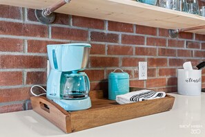 A kitchen with a brick wall, a coffee maker, a coffee pot, a mug, and a towel on a wooden tray.