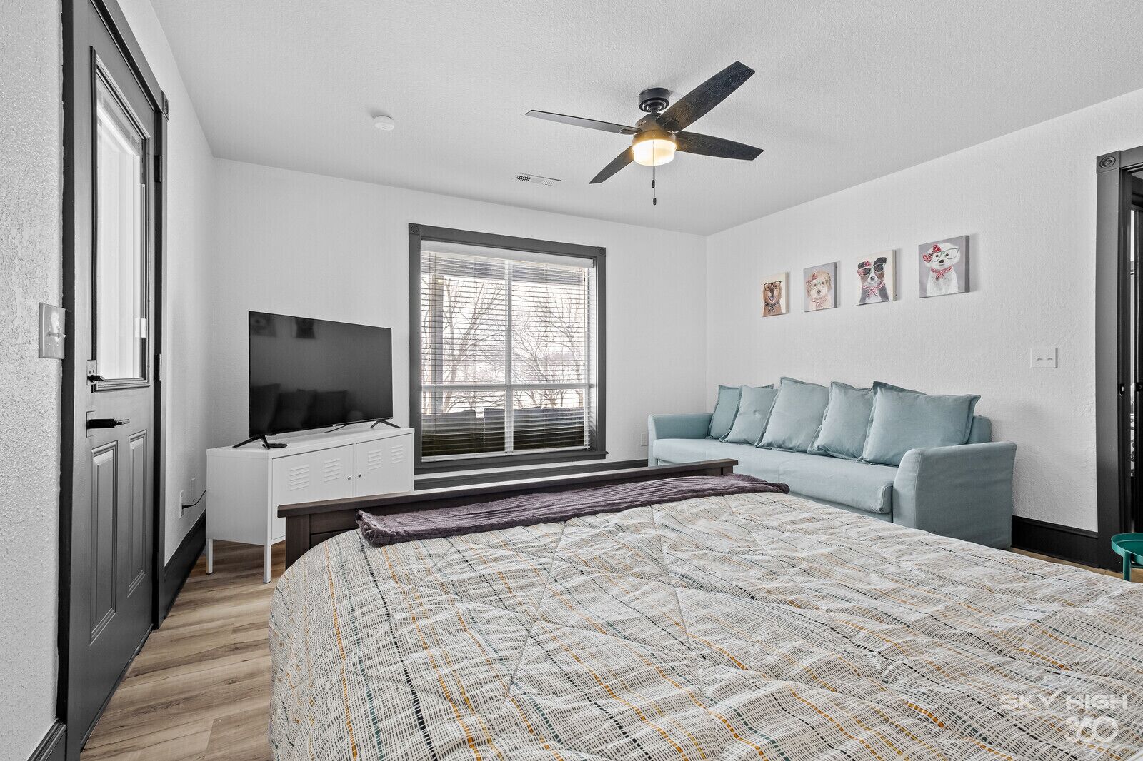 A bedroom with a bed, a TV, a ceiling fan, a window, and a light-colored wall.