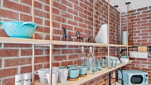 A kitchen with shelves holding various kitchenware, a microwave, and a brick wall.