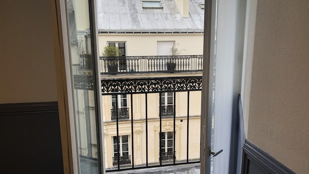 A view from a balcony with a metal railing, a wet street below, and buildings with classic architecture.