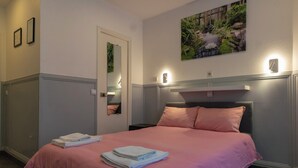 A hotel room with a bed, a nightstand, a mirror, and a wall-mounted light fixture.