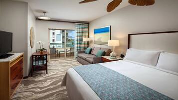 A hotel room with a bed, a desk with a TV, a dining area with chairs, and a view of the outside.
