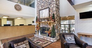Un hall con chimenea de piedra, sofás de cuero, un reloj y un televisor en la pared.