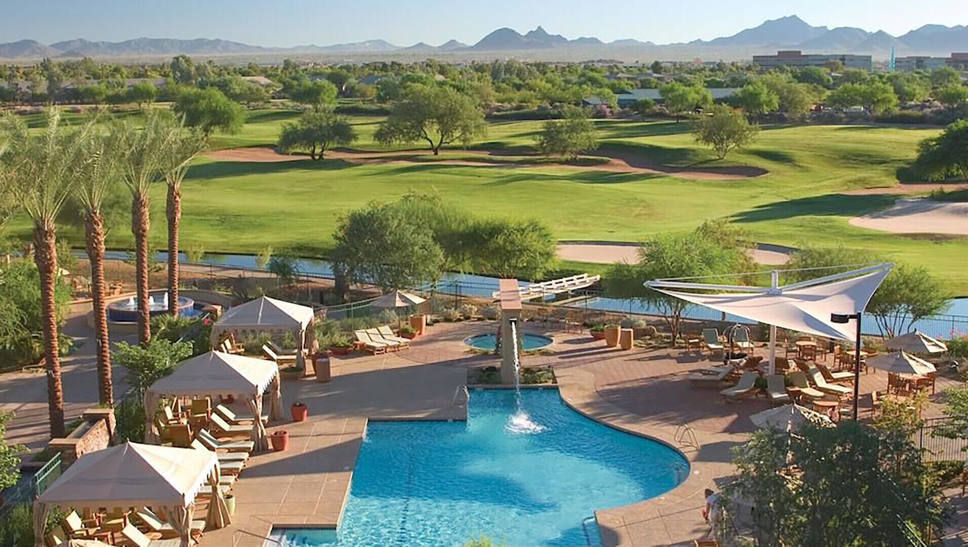 Ein Resort mit Swimmingpool, Liegestühlen und einem Golfplatz im Hintergrund.