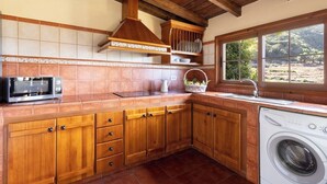 Une cuisine avec des meubles en bois, un four à micro-ondes, un lave-linge et une fenêtre donnant sur les arbres.