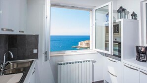 Cocina compacta con vista al mar, horno integrado y cafetera sobre la encimera.