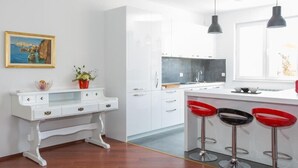 Una cocina moderna con armarios blancos, una isla central con taburetes rojos, iluminación colgante y un cuadro enmarcado en la pared.