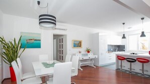 Una cocina moderna con armarios blancos, un comedor con sillas blancas y una barra con taburetes rojos.