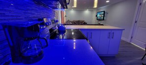 A modern kitchen with a coffee machine, a kettle, and a flat-screen TV mounted on the wall.