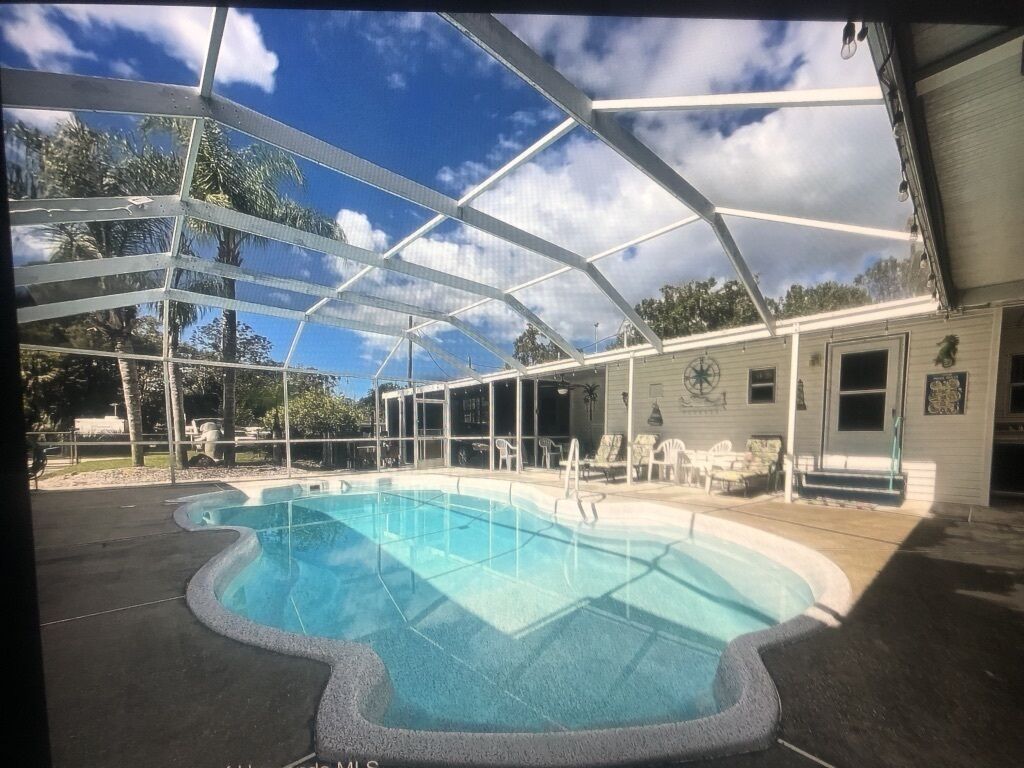 A covered outdoor swimming pool with a clear view of the sky and surrounding trees.