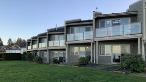 A modern multi-story residential building with balconies, large windows, and a well-maintained lawn. - Beachfront Walk-out in the Heart (Qualicum Beach)