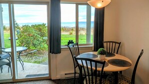 A dining area with a table and chairs, a hanging light fixture, and a view of the outdoors through large windows. - Beachfront Walk-out in the Heart (Qualicum Beach)