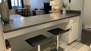A modern kitchen with a bar area, a dining table, chairs, and a large window. - Beachfront Walk-out in the Heart (Qualicum Beach)