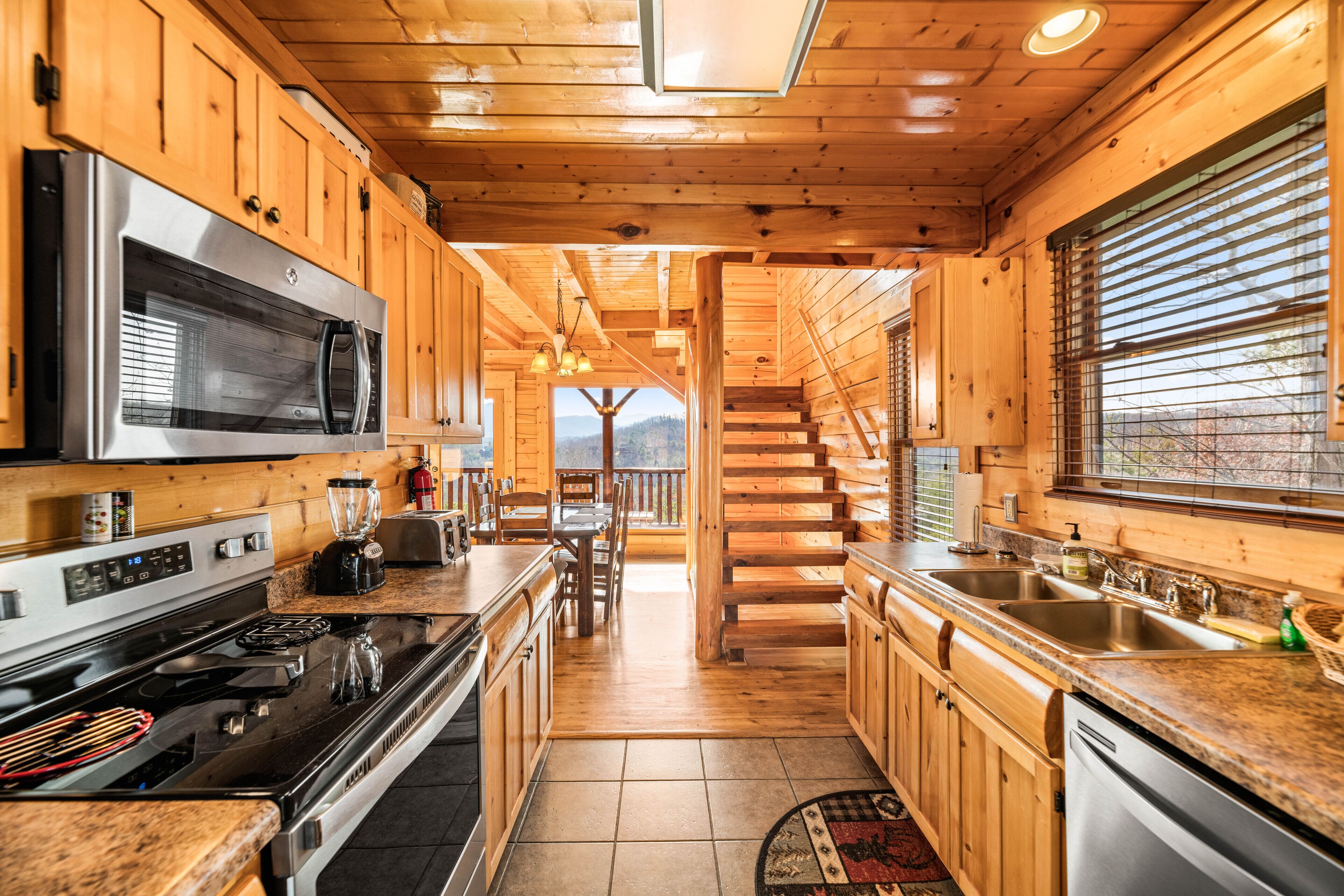 A wooden cabin kitchen with a central island, stainless steel appliances, and a view to the outside.