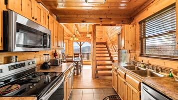 A wooden cabin kitchen with a central island, stainless steel appliances, and a view to the outside.
