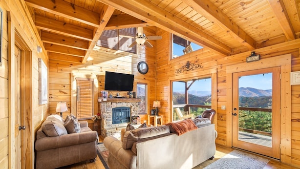 Ein Blockhaus-Interieur mit Kamin, zwei Sofas, einem Fernseher und Blick auf eine Berglandschaft.