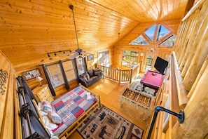 A cozy cabin interior with a loft bedroom, a dining area, and a view of the outdoors.
