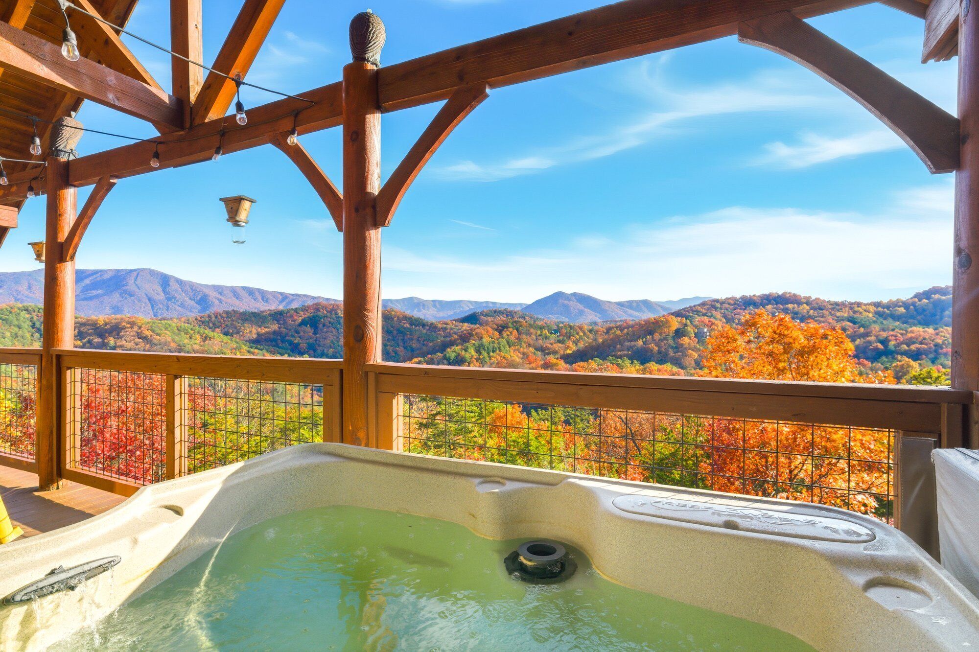 A wooden deck with a hot tub, wooden beams, and a view of autumn foliage and mountains.
