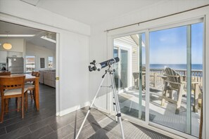 Relax in a spacious living area with a dining table, comfortable sofa, and telescope overlooking a scenic ocean view.