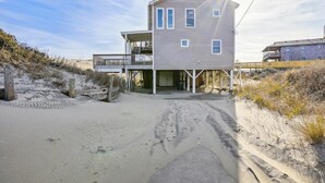 Ein zweistöckiges Strandhaus mit Balkon und überdachter Eingangsvorbau.