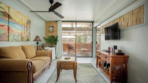 A living room with a sofa, a coffee table, a television, and a sliding glass door leading to an outdoor area. - Oceanfront Condo/Hawaiian Style. 1Bd, w/AC & Wifi (Kailua-Kona)